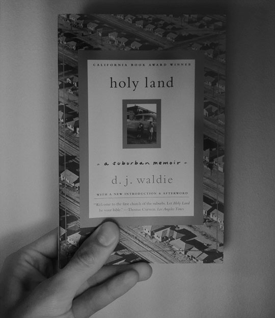 image of the book, holy land, held up with one hand for scale.