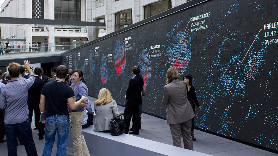 people milling in front of a wall showing air quality as dancing motes of light